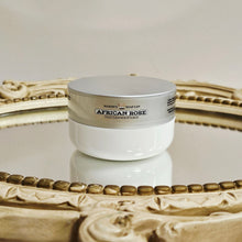 Load image into Gallery viewer, White jar with silver lid labeled 'African Rose' on a decorative mirror.