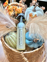 Load image into Gallery viewer, Blackberry Harvest luxury body oil displayed in a fall basket with pumpkins and flowers.