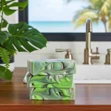 Load image into Gallery viewer, Three stacked rectangular bars of soap with a green, lime, and dark gray marbled pattern, displayed on a wooden countertop in a kitchen setting with a sink and a window view of a beach in the background.