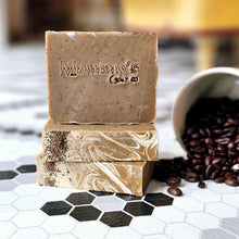 Load image into Gallery viewer, Stack of beige coffee-themed soap bars with a swirl pattern, branded with 'Mammy's Soap Co.' logo, alongside a cup of coffee beans.