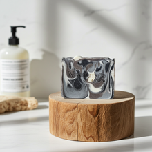Load image into Gallery viewer, A rectangular bar of soap with a black, white, and gray marbled swirl pattern sits on a round wooden block. The soap has 'Mammy's Soap Co' embossed on the front.