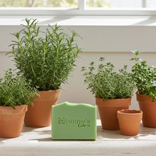 Load image into Gallery viewer, a bar of green soap on a table surrounded by pots of herbs