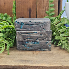Load image into Gallery viewer, Three bars of soap with a wavy pattern on a wooden surface with greenery in the background