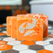 Load image into Gallery viewer, Four orange and white marbled handmade soap bars stacked on a hexagonal tile surface. The front soap is embossed with the brand name 'Mammy's Soap Co'.