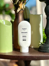 Load image into Gallery viewer, Haughty Hand Lotion displayed on a wooden table beside green candles, a vase, and black décor.