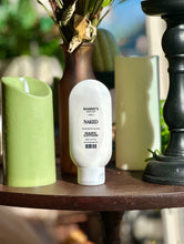 Load image into Gallery viewer, Naked Hand Lotion displayed on a wooden table beside green candles, a brown vase, and black décor.