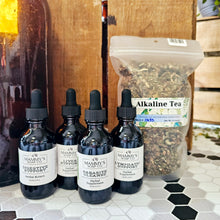 Load image into Gallery viewer, A selection of herbal tinctures and a bag of loose tea leaves, labeled 'Alkaline Tea', on a kitchen countertop.