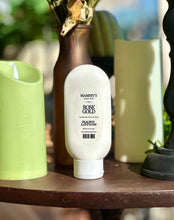 Load image into Gallery viewer, Rose Gold Hand Lotion displayed on a wooden table beside green candles, a brown vase, and black décor.