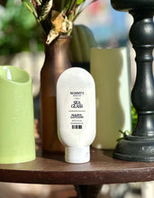 Load image into Gallery viewer, Sea Glass Hand Lotion displayed on a wooden table beside green candles, a brown vase, and black décor.