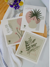 Load image into Gallery viewer, Set of 3 Swedish dishcloths with botanical and plant designs on a wooden surface