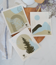 Load image into Gallery viewer, Set of 3 nature-themed Swedish dishcloths on a wooden surface with a white towel and lavender flowers.