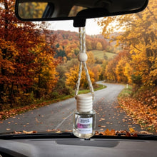 Load image into Gallery viewer, A hanging car air freshener bottle labeled 'Mammy's Soap Co Sweet Fig' suspended from a rearview mirror inside a car, with a scenic autumn road and trees visible through the windshield.