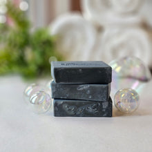 Load image into Gallery viewer, Stack of three rectangular navy soaps with a textured surface, displayed in front of a blurred background featuring greenery and more soap bubbles.