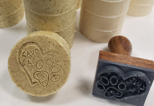 Load image into Gallery viewer, round tan bar soap with tan specks stamped with heart and paw print Save A Life with stamp and soap bars in stacked in back