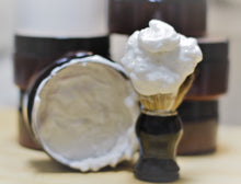 Load image into Gallery viewer, shaving brush with black handle topped with shaving soap lather and open used shaving soap jar in background