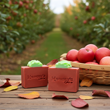 Load image into Gallery viewer, two bars of red and green soap on a wood table next to a basket of apples in an orchard
