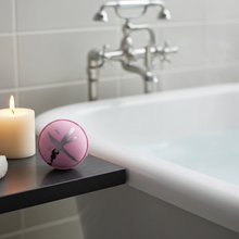 Load image into Gallery viewer, Pink and silver bath bomb on a ledge next to a candle in a bathroom.
