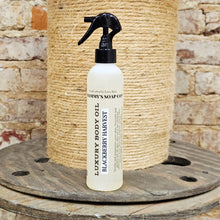 Load image into Gallery viewer, White spray bottle with black nozzle labeled 'Luxury Body Oil' on a wooden surface with a stone wall background.
