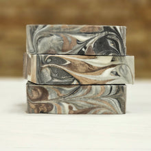 Load image into Gallery viewer, Three bars of white, black, brown and black soap on a white surface
