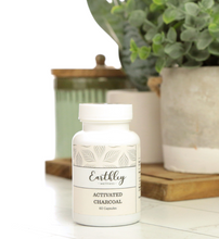Load image into Gallery viewer, Earthley Activated Charcoal supplement bottle on a white surface with plants in the background
