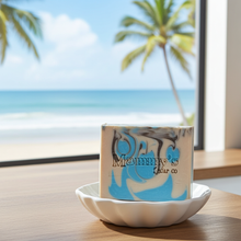 Load image into Gallery viewer, A rectangular bar of soap with a blue, white, and gray marbled pattern sits on a white scalloped dish. The soap is printed with the brand name 'Mammy's Soap Co'.
