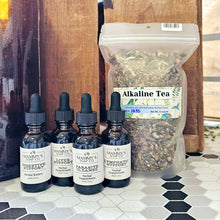 Load image into Gallery viewer, A selection of glass bottles with black dropper caps labeled with different tincture names, arranged in a row in front of a clear plastic bag labeled 'Alkaline Tea'. The bottles are on a tiled surface with a wooden cabinet in the background.
