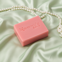 Load image into Gallery viewer, A pink rectangular bar of soap with 'Mammy's Soap Co' embossed on top, styled on a draped light green satin fabric with a strand of white pearls.
