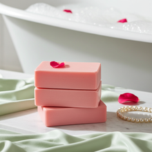 Load image into Gallery viewer, Three stacked pink soap bars on a marble surface with a white bathtub filled with bubbles in the background, accented by pink rose petals and a pearl bracelet.
