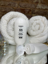Load image into Gallery viewer, Two squeeze bottles of hand lotion in front of white folded towels on a textured surface
