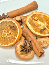 Load image into Gallery viewer, A close-up arrangement of dried spices and citrus on a white surface, including two dried orange slices, two cinnamon sticks, star anise, and a dried apple slice with cloves.
