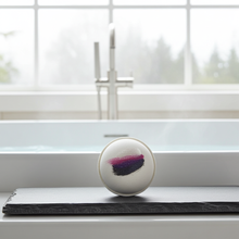 Load image into Gallery viewer, Round bath bomb with purple design on a surface in front of a window
