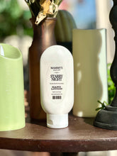 Load image into Gallery viewer, Starry Night Hand Lotion displayed beside green candles, a brown vase, and black décor.
