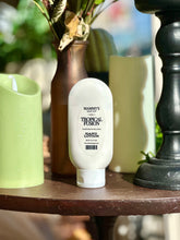 Load image into Gallery viewer, Tropical Fusion Hand Lotion displayed on a wooden table beside green candles, a brown vase, and black décor.
