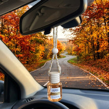 Load image into Gallery viewer, A small clear glass car air freshener bottle with a white cap hangs from a white cord under the rearview mirror inside a car. The bottle label reads 'Mammy's Soap Co Vanilla Oak'
