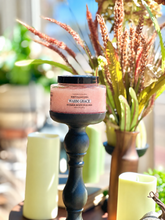 Load image into Gallery viewer, Warm Grace Sugar Body Polish displayed on a black pedestal among green candles and fall florals.
