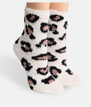 Load image into Gallery viewer, A pair of plush, fuzzy crew socks with a leopard print pattern in black and dusty pink on an off-white background, shown on a light gray studio background.
