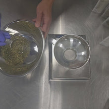Load and play video in Gallery viewer, Blending of Moringa Mint Herbal Tea with dried leaves and flowers in a stainless steel bowl on a stainless steel table, pouring into a compostable pouch.
