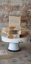 Load image into Gallery viewer, cream colored handmade bar soap with oats and honeycomb look stacked on vintage metal pedestal with old brick wall background

