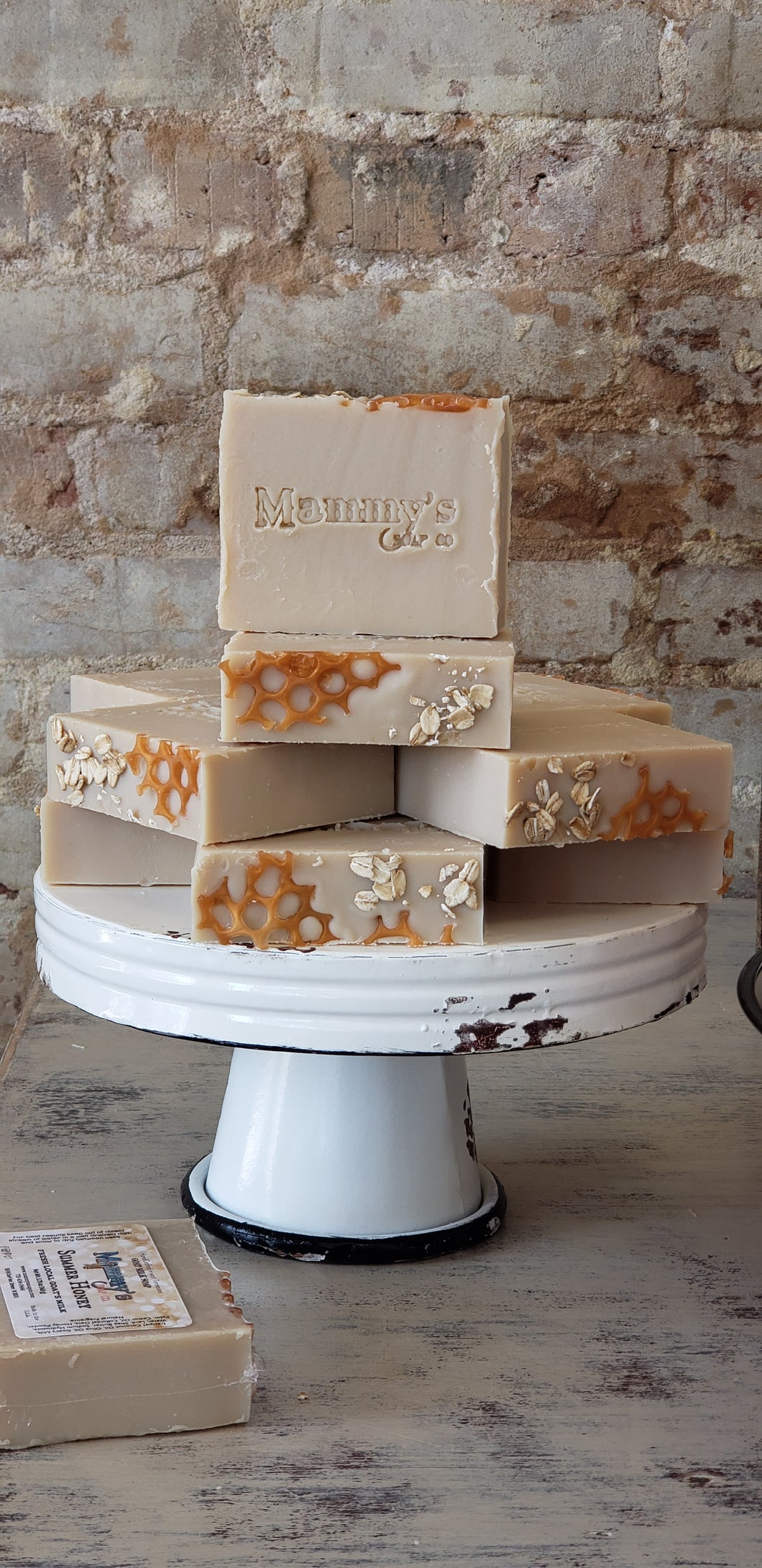 cream colored handmade bar soap with oats and honeycomb look stacked on vintage metal pedestal with old brick wall background