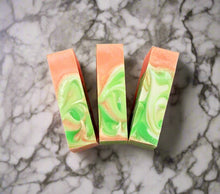 Load image into Gallery viewer, Three bars of orange, green and white soap tops on a marbled surface. 
